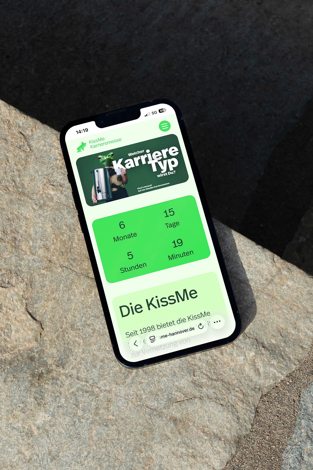 Ein iPhone liegt auf einem Untergrund auf Stein. Auf dem Display ist die Startseite der KissMe Karrieremesse geöffnet.
