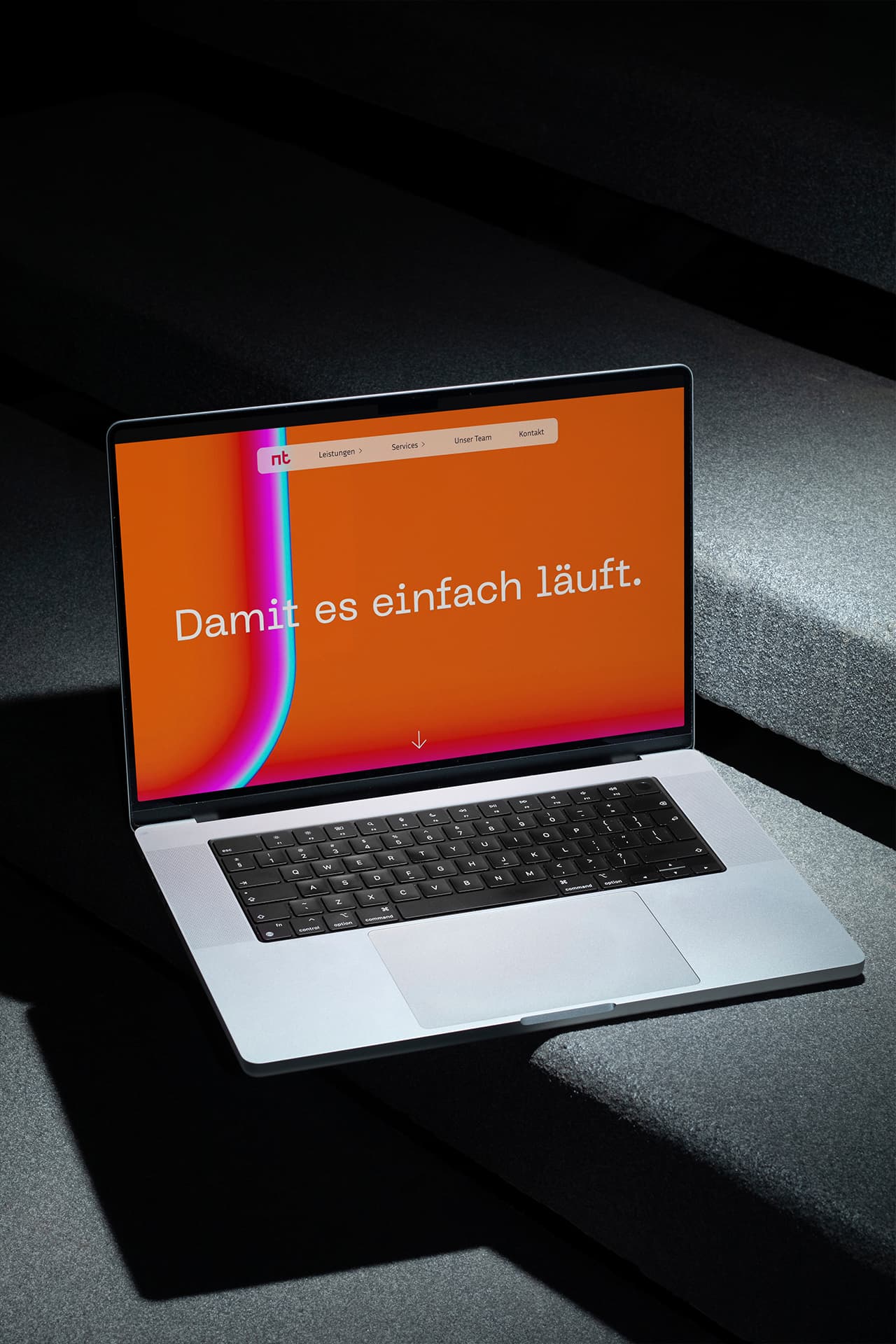 Ein MacBook steht auf einer Treppenstufe aus Stein. Auf dem Bildschirm sieht man die Startseite der Webseite der NT Hannover.