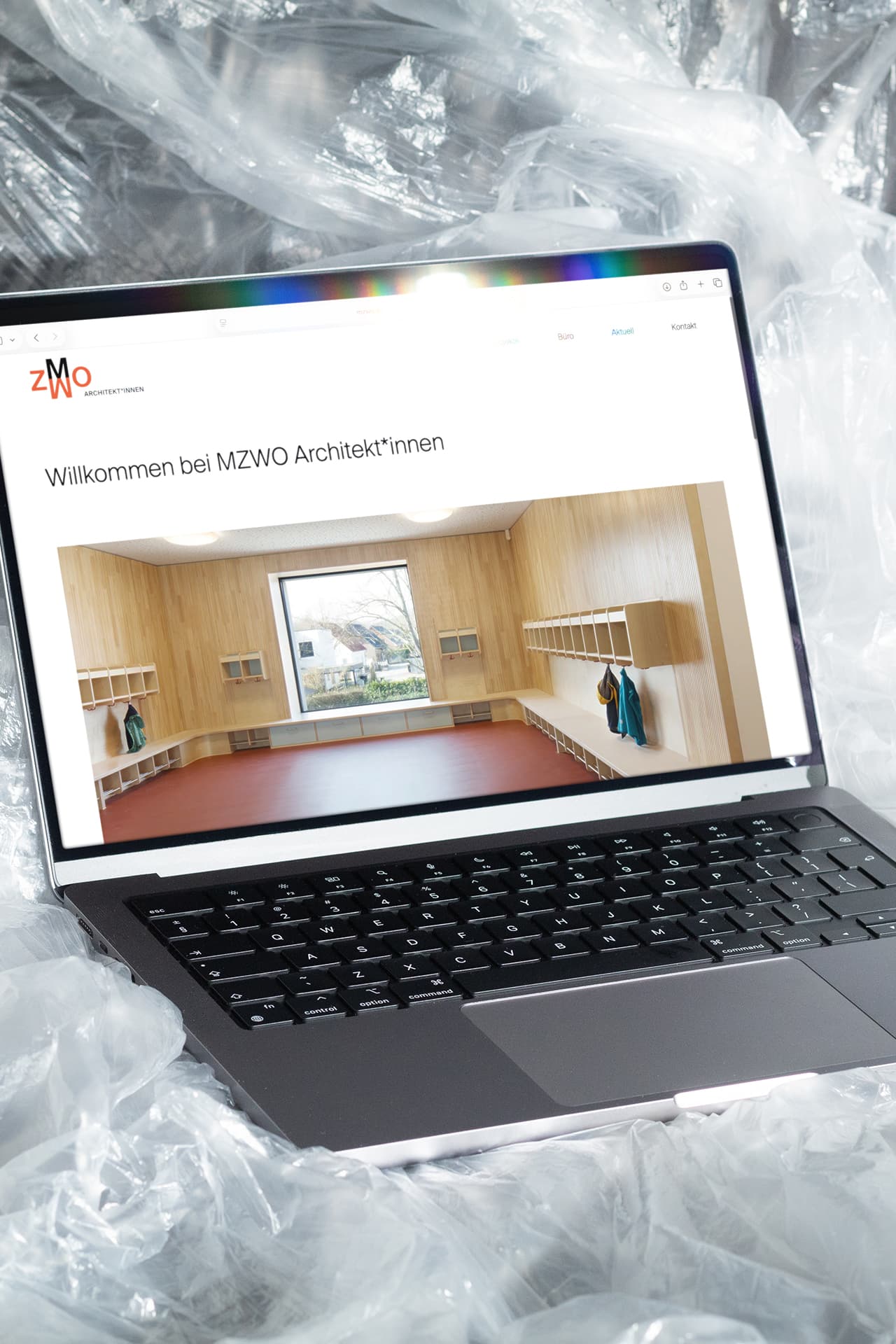 Ein MacBook ist teilweise eingewickelt in einer Plastikfolie. Auf dem Bildschirm sieht man die Startseite der Webseite von MZWO Architekt*innen.